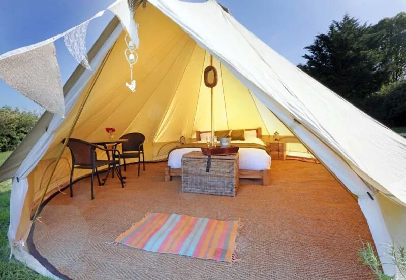 Inside one of the glamping bell tents — a made-up double bed, rug and chairs